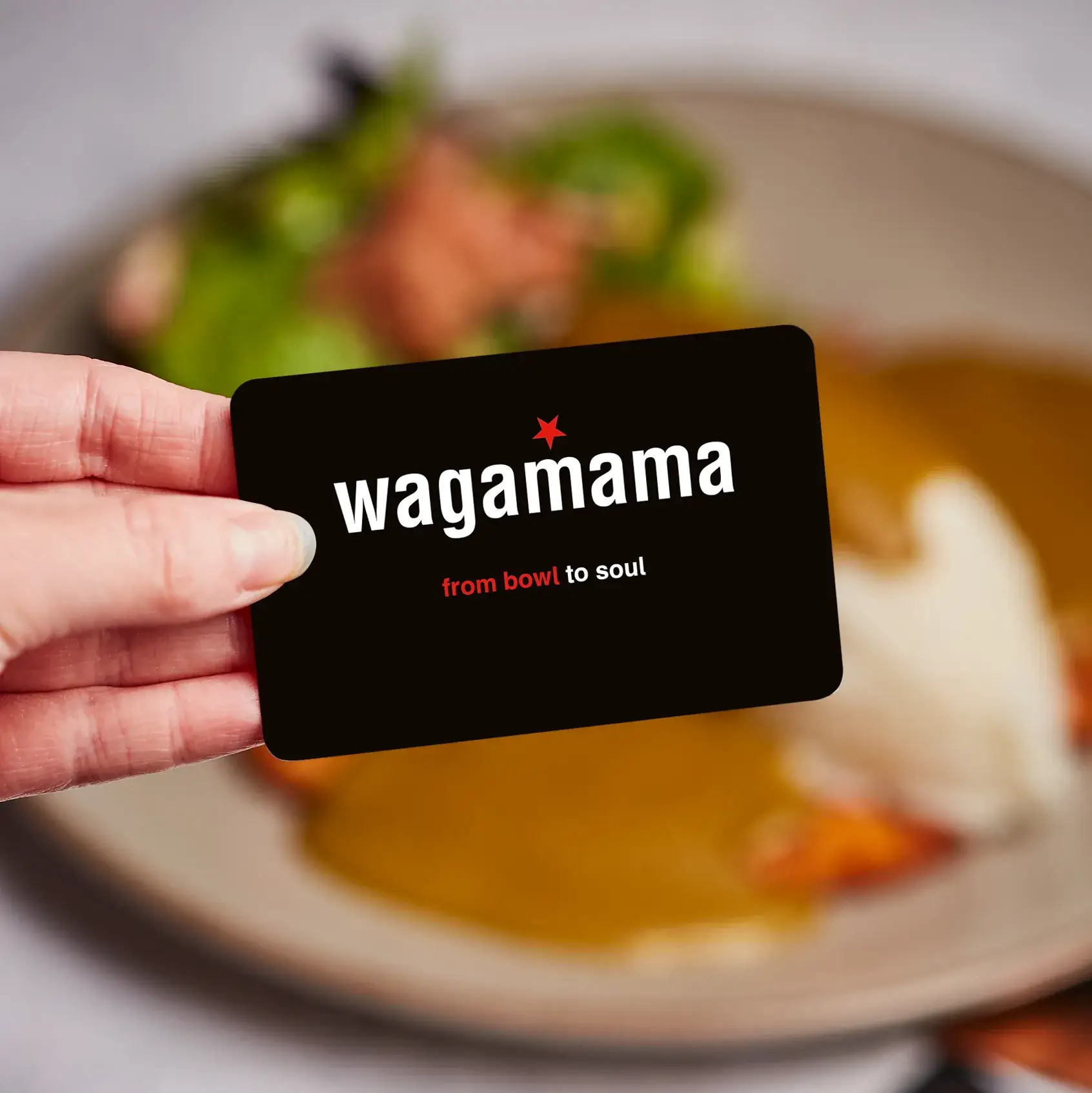 hand holding wagamama gift card in front of chicken katsu curry