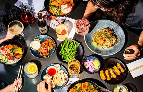 a table full of delicious wagamama food and drink being enjoyed by a group of friends