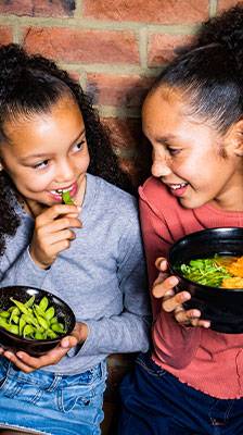 2 girls hold black bowls with edamame and ramen Custom data
